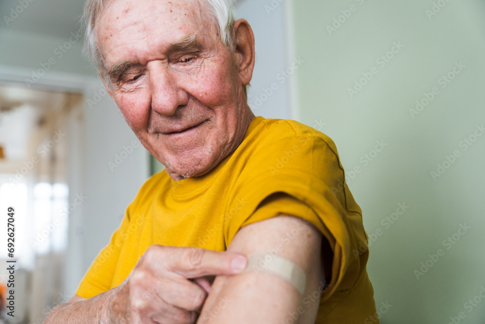 Happy old grandfather at his home. An adult pensioner sits against a wall with a bandage after vaccination. Happy old grandfather at his home. An adult pensioner sits against a wall with a bandage after vaccination.