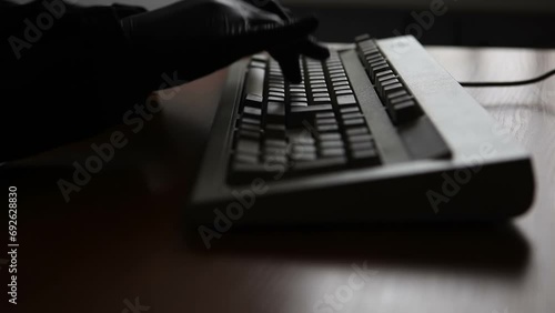 An unknown anonymous man in a black jacket and black gloves is typing a message on a computer keyboard. Video with sound. photo