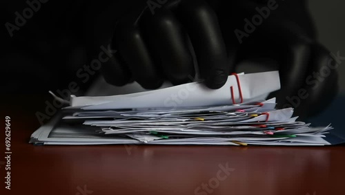 An unknown man in black gloves is rummaging through other people's documents lying on the table. A criminal is going through a folder of papers in someone else's office.