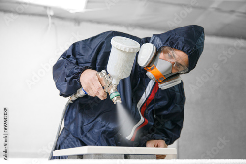 Professional worker staining wood furniture with spray gun