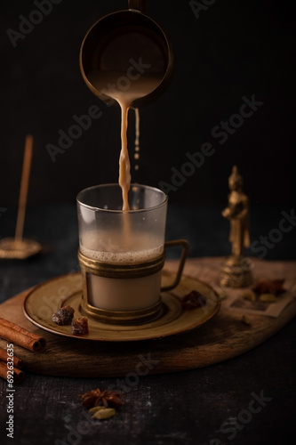 Indian masala chai with spices, brown sugar and cinnamon sticks. Hot masala tea is poured into a glass with steam.