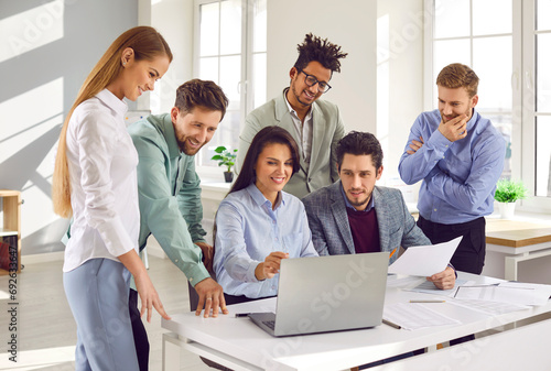 Team of business people using a modern computer during a work meeting in the office. Group of happy diverse men and women looking at the laptop on the desk photo
