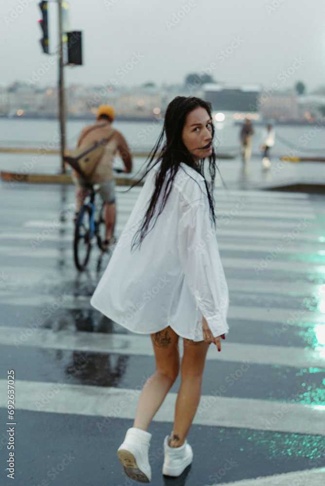 Woman walking down street in rainy weather in white shirt and blue jeans shorts