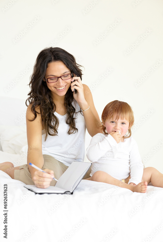 Phone call, writing and a single mother with her baby in the bedroom of a home, planning to multitask. Book, family or kids with book with a happy young woman and her infant child sitting on a bed Phone call, writing and a single mother with her baby in the bedroom of a home, planning to multitask. Book, family or kids with book with a happy young woman and her infant child sitting on a bed