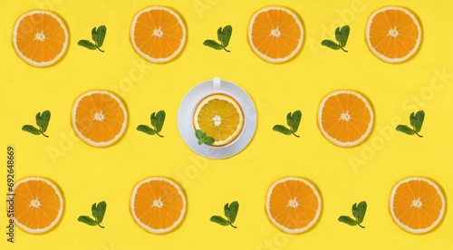 Half a orange, mint leaves and tea cup on the yellow background. Pattern. Flat lay. Creative food collage.