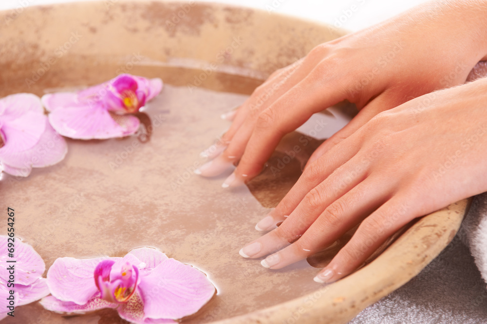 Woman, hands and water for manicure, skincare or cosmetics in zen, beauty or salon and spa treatment. Closeup of female person resting nails in bowl of natural mineral liquid with flowers in wellness