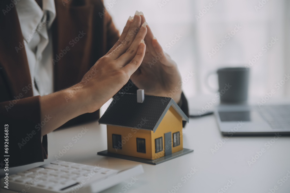 Female hands saving small house with a roof Female hands saving small house with a roof