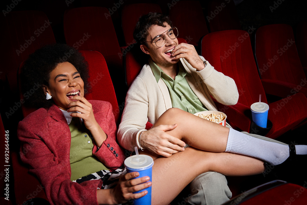 handsome man with glasses with his arm or leg of his joyous african american girlfriend at cinema handsome man with glasses with his arm or leg of his joyous african american girlfriend at cinema