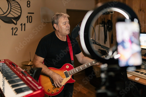 Canvas Print Mature male musician singing and playing guitar in studio