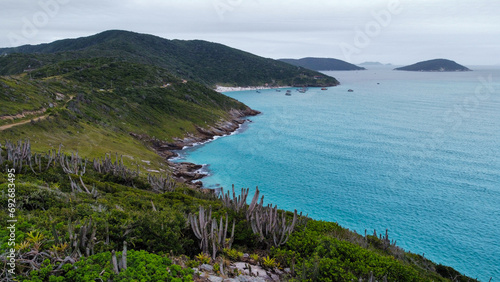 Cliff on the ocean in Arraial do Cabo, Brazil. Beautiful natural colors with blue ocean, waves that become foam, green hills.