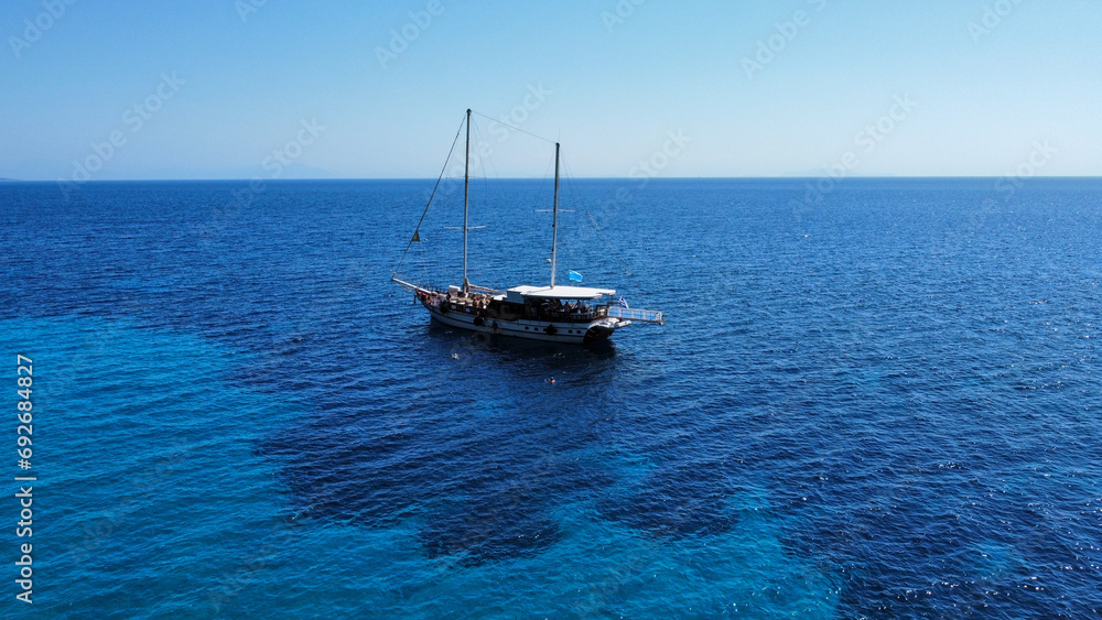 Fototapeta premium Sailing boat (caique) in Greece; Crystal water, beautiful colors and shades of blue. In the background the island