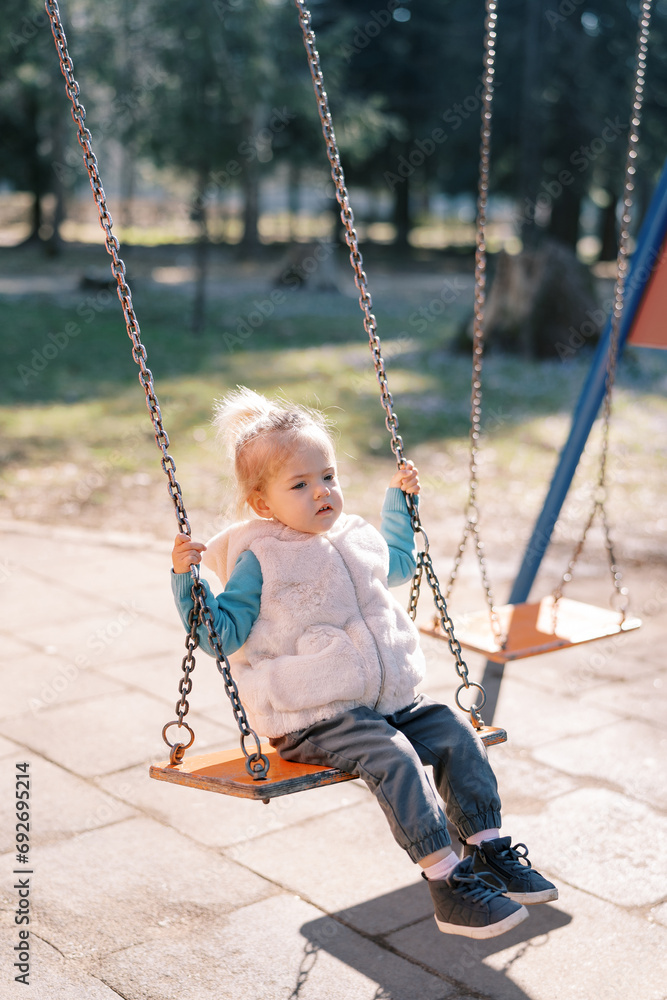 Little girl swings on a chain swing in a spring park