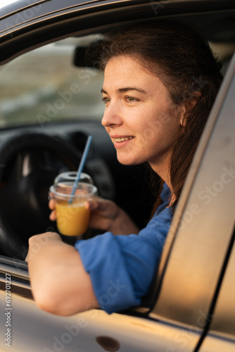 Happy young woman with cocktail driving her car. Woman sipping a cold juice while in car. Young driver drinking beverage