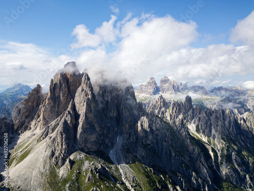 Aerial view of Cadini di Misurina mountains with Tre Cime di Lavaredo mountains in the background during a sunny day with some clouds. Dolomites, Italy. Dramatic and cinematic landscape.