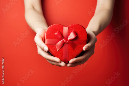 Woman s hands with a heart-shaped gift box against a red backdrop