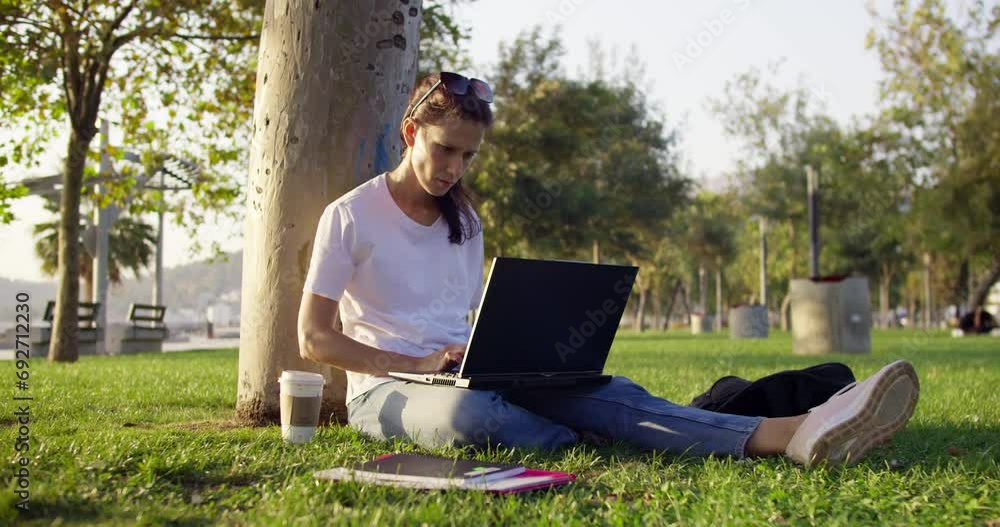 Female student online lesson making notes in copybook sitting sunny park. University student doing homework using laptop for studying in campus area Female student online lesson making notes in copybook sitting sunny park. University student doing homework using laptop for studying in campus area