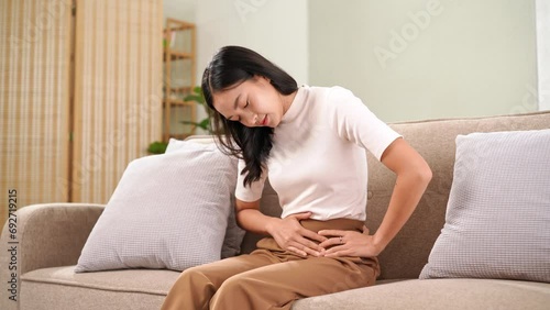 Young asian woman sitting on sofa having painful stomach ache, Menstrual period cramp, food poisoning photo