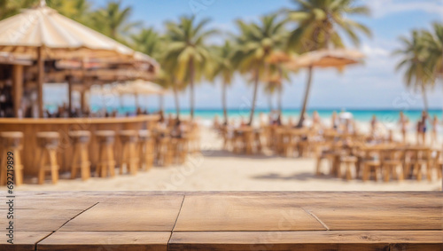 An empty wooden plank table on a blurred background of a sunny beach with sea palm trees and vacationing people near a cafe and bar