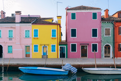 The vividly painted houses of Burano, Venice reflect in the still canal water, under a clear blue sky photo