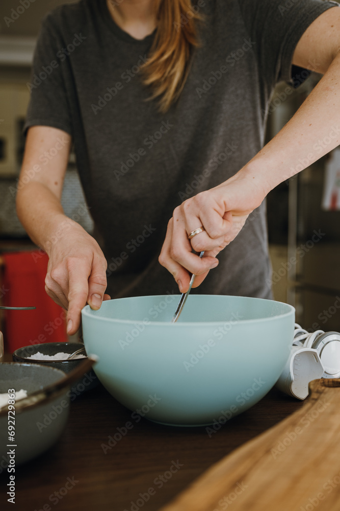 Women's hands mixing ingredients in bowl.
