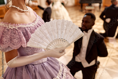 Closeup of beautiful renaissance lady holding fan during ball reception in palace, copy space photo