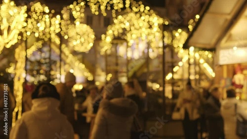 Blurred illuminated Christmas market. People hanging out at Christmas market. Shimmering garlands. Defocused people drink mulled wine and walking. Winter activities. Beautifully illuminated fair photo