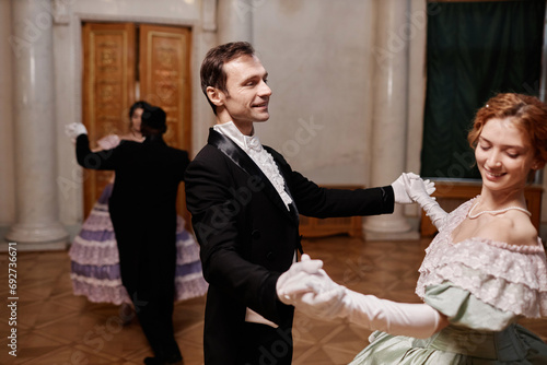 Portrait of smiling gentleman wearing classic tailcoat dancing with young lady during debutante ball in palace, copy space