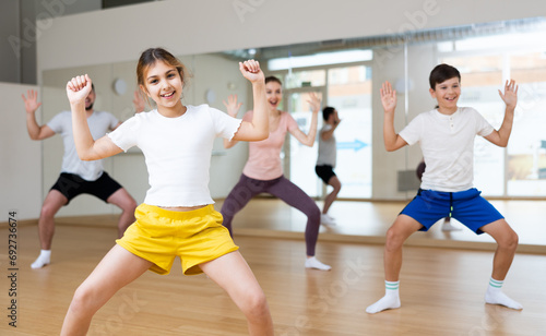 Portrait of happy preteen girl practicing dynamic synchronous choreography with her family in modern dance studio..