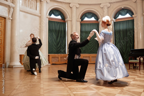Full length of renaissance couples dancing in palace ballroom with ladies swirling around gentlemen partners, copy space photo