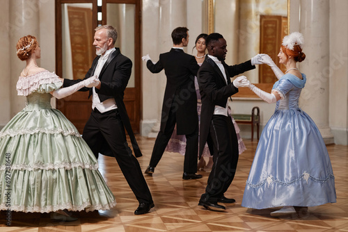 Fotografie, Obraz Full length portrait of three couples dancing waltz in classic palace ballroom,