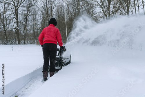 A young woman clears snow with snow removal equipment after a heavy snowfall
