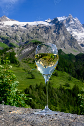 Drinking of dry white Roussette de Savoie and Vin de Savoie wine from Savoy region with view on Hautes Alpes mountains with snow on tops in summer