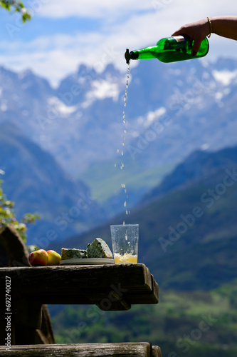 Pouring from high height of natural Asturian cider made from fermented apples, Asturian cabrales cow blue cheese with view on Naranjo de Bulnes top of Picos de Europa mountains, Spain photo