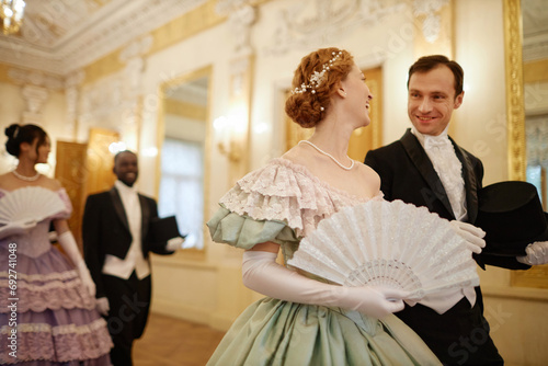 Waist up portrait of elegant couple of lady and gentleman chatting cheerfully walking in palace hall photo