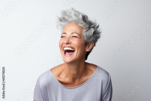 Portrait of a happy senior woman with grey hair laughing against grey background © Loli