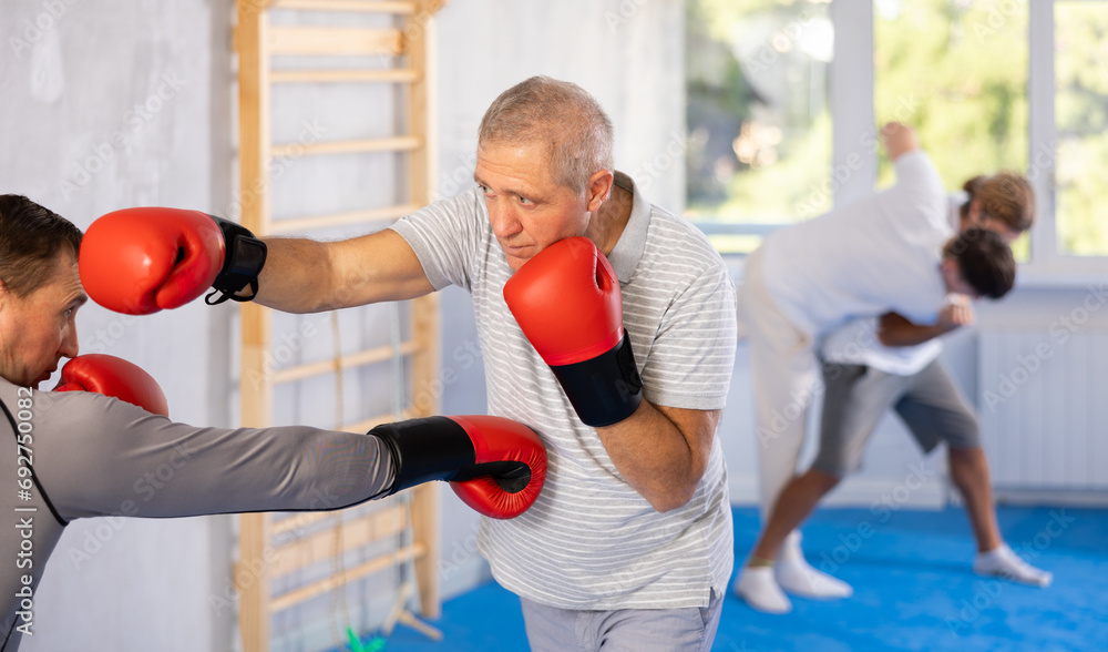 Elderly man and adult men in boxing gloves boxing in gym..