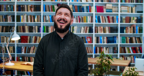 Portrait of cheerful Caucasian man looking to camera and smiling in library. Male customer or joyful worker laughing in bibliotheca. Books shelves on background. Senior smiled teacher.
