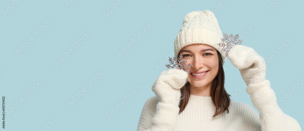Pretty young woman in warm clothes holding decorative snowflakes on light blue background with space for text Pretty young woman in warm clothes holding decorative snowflakes on light blue background with space for text