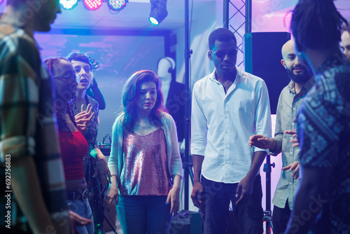 Young friends chatting while partying on dancefloor and improvising dance battle in crowded nightclub. Diverse people having fun and talking while clubbing and celebrating