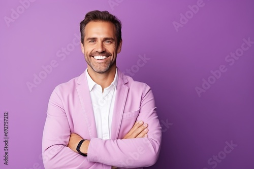 Portrait of a smiling young man standing with arms folded against purple background