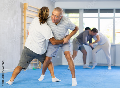 Adult man and elderly men judokas practicing judo technique in gym..