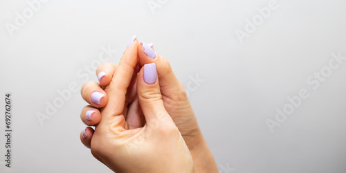 Female hands with a chip on a homemade purple gel polish manicure against a light wall
