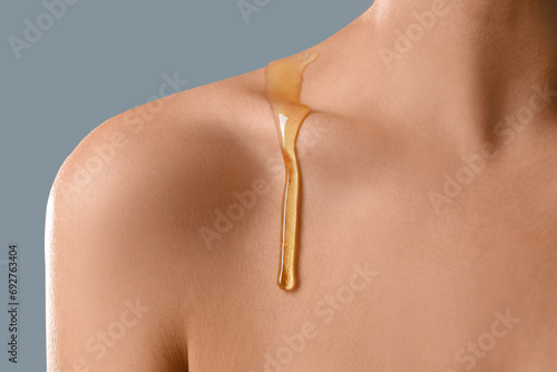 Young woman with dripping honey on collarbone against grey background, closeup photo