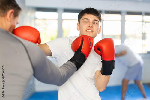 Man and guy in boxing gloves punch deliver blow each other during training sparring session. Practical use of technique and force of impact in combat practice. © JackF