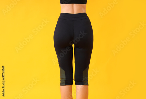 Young woman in black cycling shorts on yellow background, back view photo