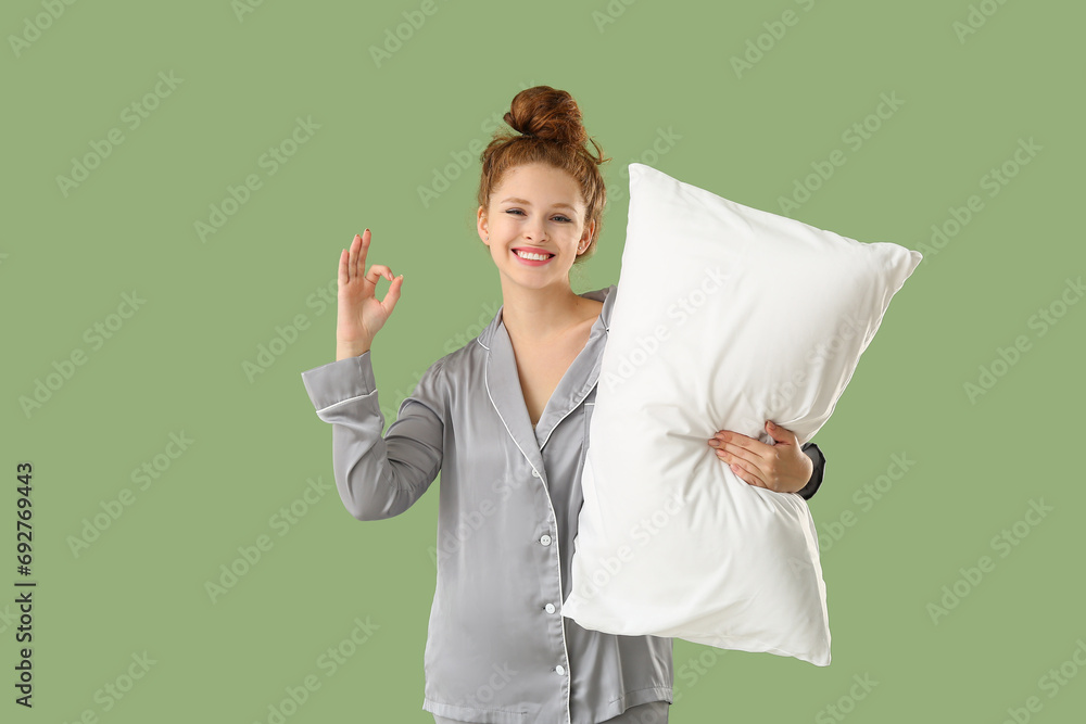 Beautiful young woman holding white soft pillow and showing ok gesture on green background Beautiful young woman holding white soft pillow and showing ok gesture on green background