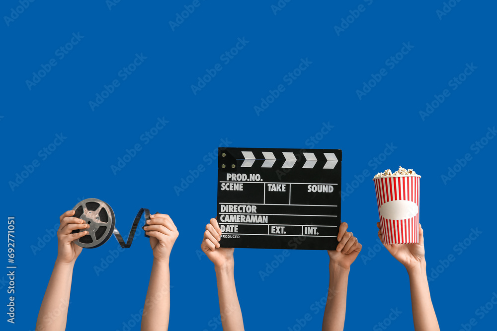 Female hands with movie clapper, reel and bucket of popcorn on blue background - obrazy, fototapety, plakaty 