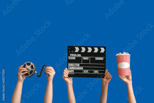 Female hands with movie clapper, reel and bucket of popcorn on blue background photo