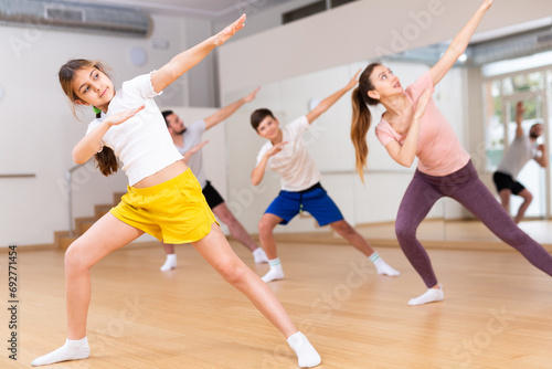 Girl practising dance moves with parents and sibling in dancing room.