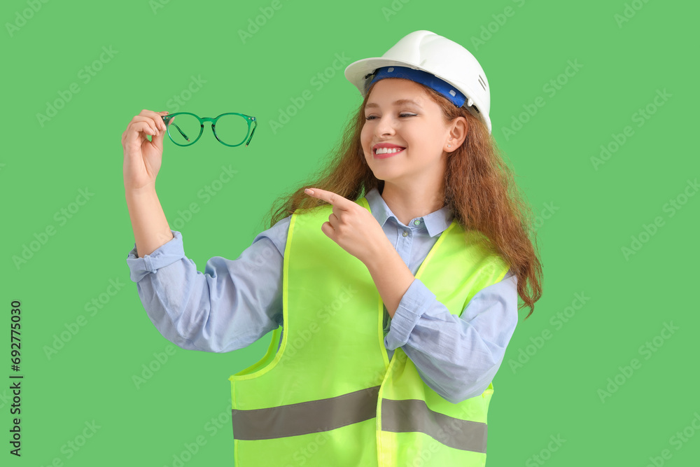 Female construction worker pointing at eyeglasses on green background Female construction worker pointing at eyeglasses on green background